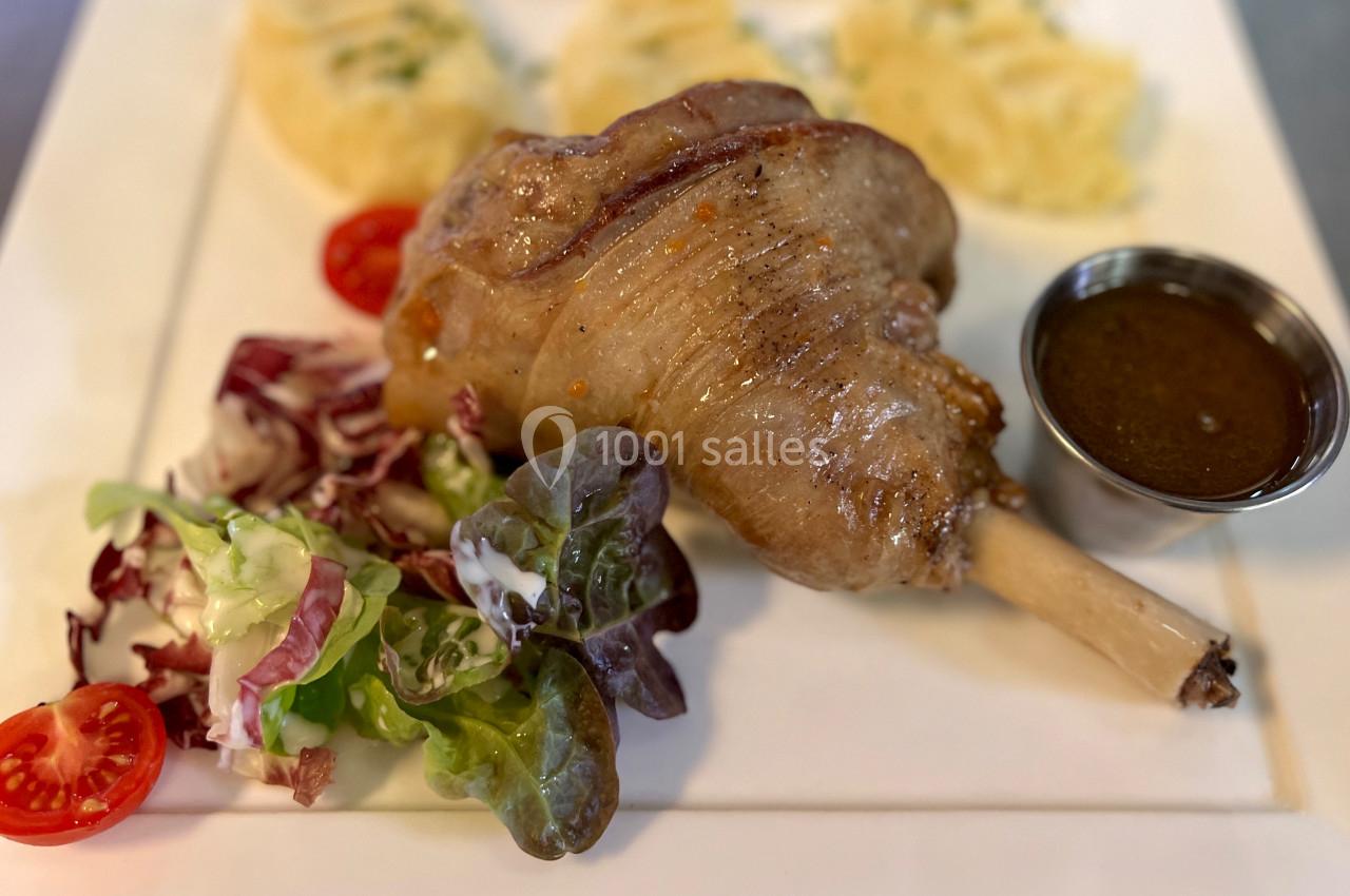 Plat avec un jarret d'agneau rôti, purée de pommes de terre, salade verte et tomates cerises, sauce servie à part.