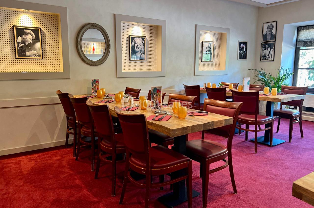 Salle de restaurant avec tables en bois, chaises rouges, décorations murales et lumière naturelle provenant d'une fenêtre.