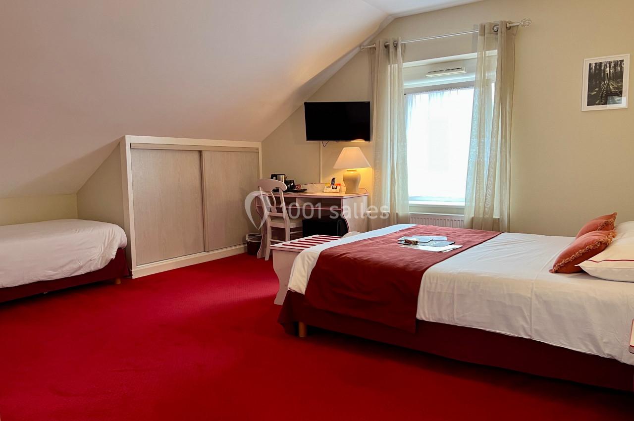 Chambre lumineuse avec lit double, lit simple, bureau, télévision murale et moquette rouge.