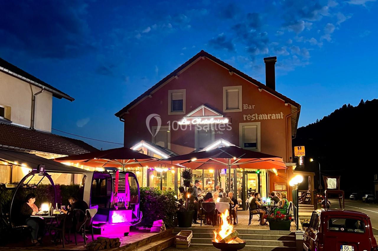 Terrasse d'un restaurant éclairée en soirée, avec des clients attablés et un brasero au premier plan.