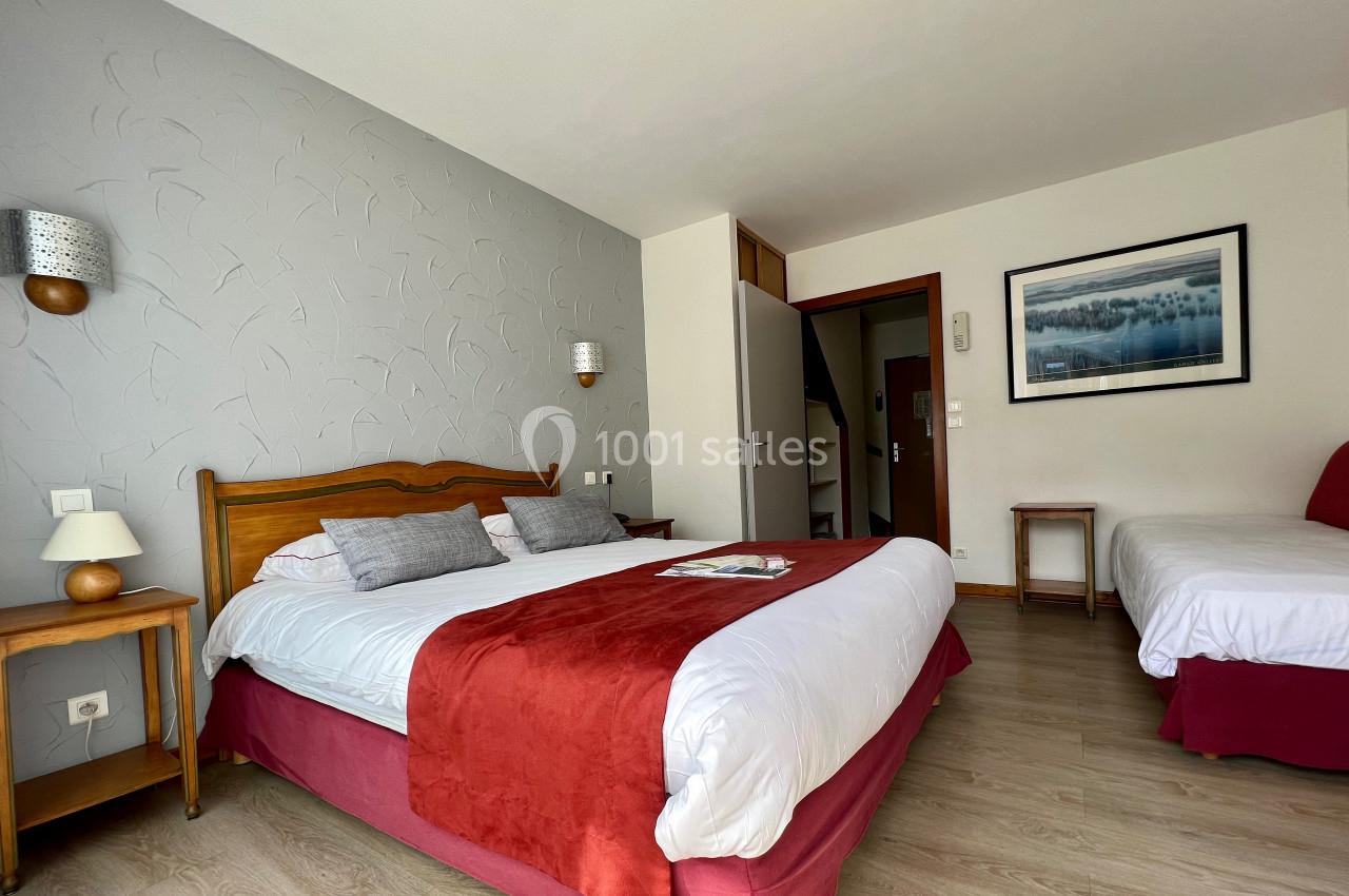 Chambre lumineuse avec un lit double, un lit simple, des tables de chevet et un tableau au mur.