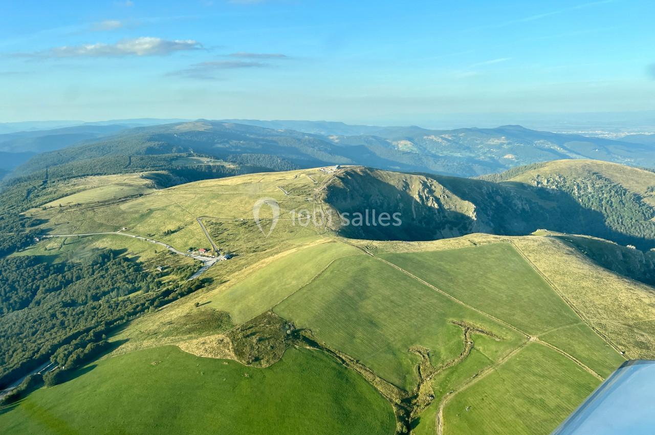 Vue aérienne de collines verdoyantes et vallonnées sous un ciel bleu dégagé.