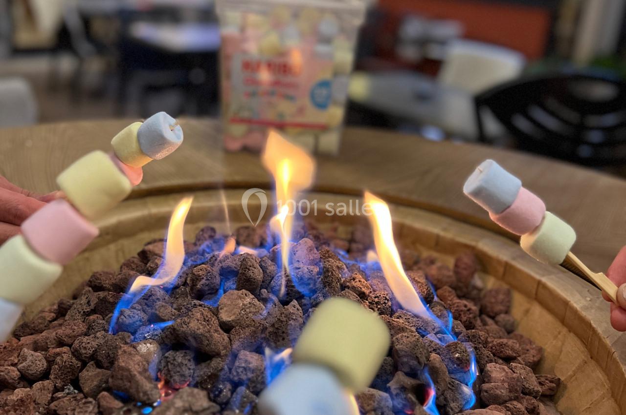 Des guimauves colorées sont grillées sur un feu de table entouré de pierres volcaniques dans un cadre convivial.