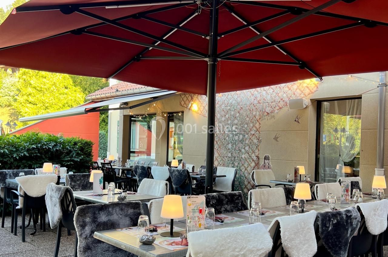Terrasse de restaurant avec tables dressées, chaises couvertes de plaids et grands parasols rouges.