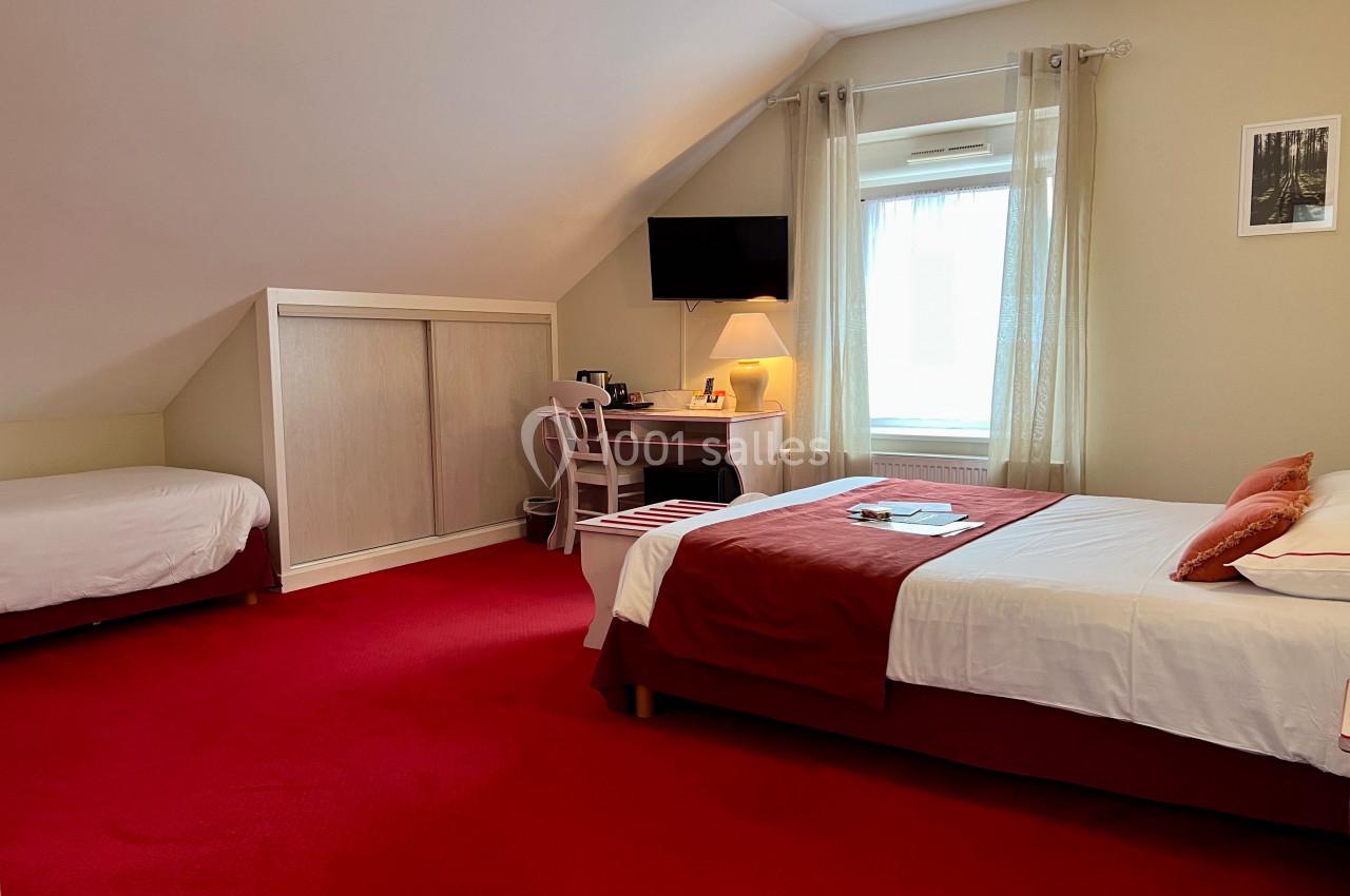 Chambre mansardée avec deux lits, un bureau, une télévision murale et une fenêtre laissant entrer la lumière naturelle.