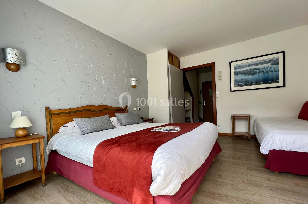 Chambre lumineuse avec un lit double, un lit simple, des tables de chevet et un tableau encadré au mur.