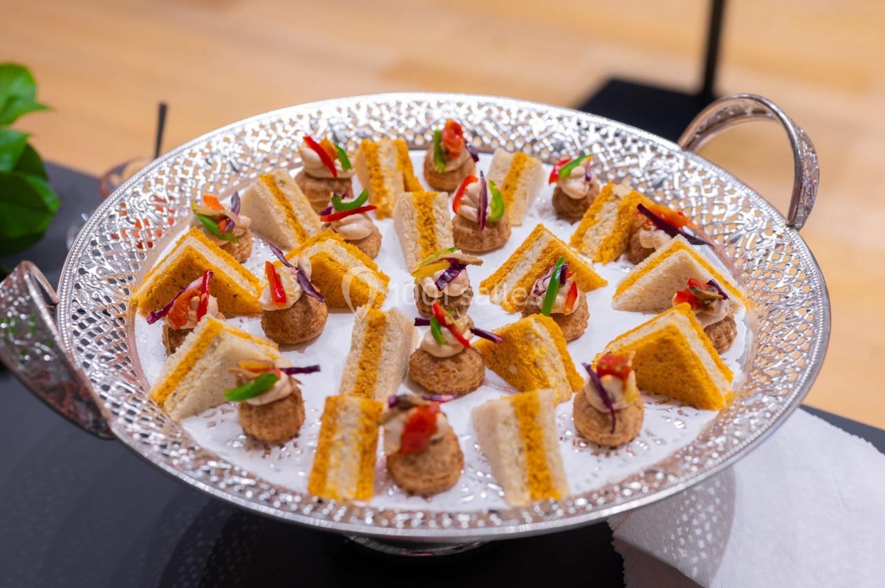 Plateau argenté contenant des mini-sandwichs triangulaires et des bouchées garnies de légumes colorés.