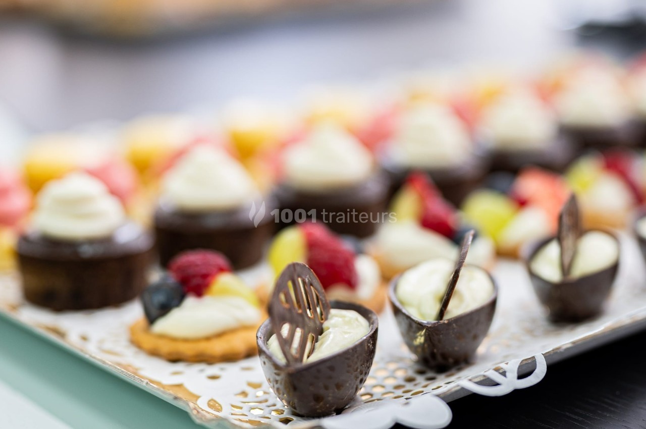 Assortiment de desserts miniatures, incluant tartelettes aux fruits et coupes en chocolat garnies de crème.