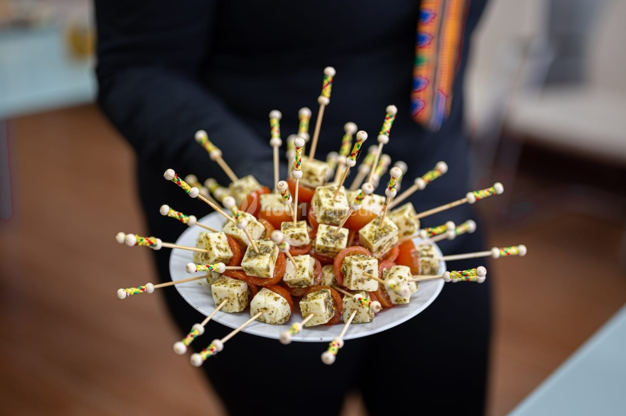 Assiette de brochettes apéritives avec cubes de fromage aux herbes et tomates cerises, tenue par une personne.