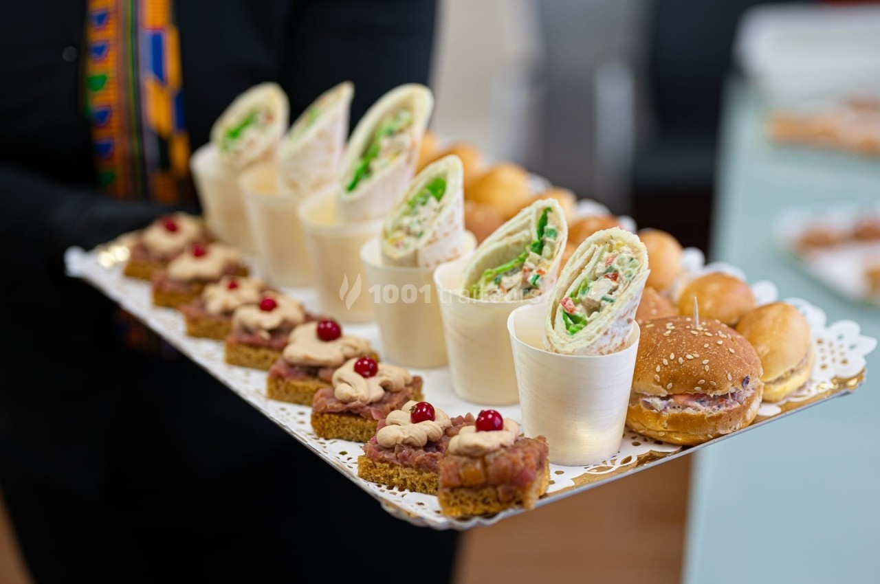 Plateau de bouchées variées comprenant wraps, mini-sandwichs et toasts garnis, présenté sur un support décoratif.