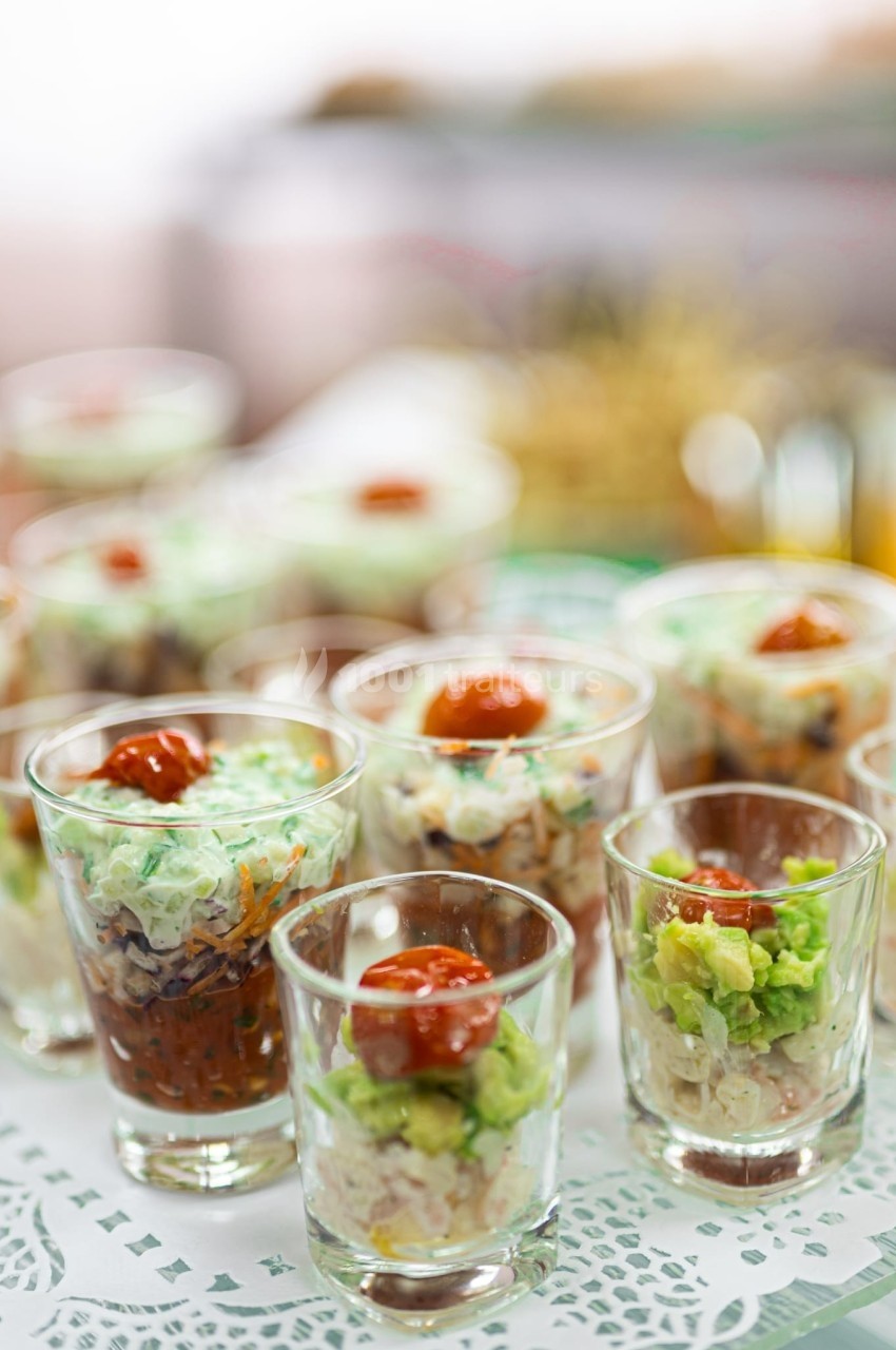Verrines variées contenant des ingrédients colorés comme avocat, sauce rouge et légumes, disposées sur une nappe blanche.