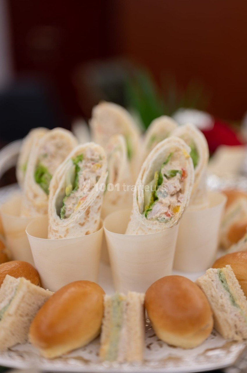 Assortiment de wraps garnis de légumes et de poulet, entourés de petits pains et de sandwichs sur un plateau.