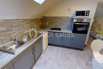 Salle de bain moderne avec douche vitrée, lavabo blanc, miroir, sèche-serviettes et poutres en bois apparentes.