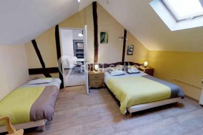 Salle de bain moderne avec douche vitrée, lavabo blanc, miroir, sèche-serviettes et poutres en bois apparentes.