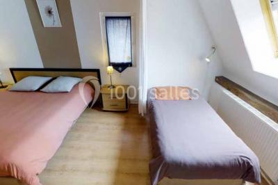 Salle de bain moderne avec douche vitrée, lavabo blanc, miroir, sèche-serviettes et poutres en bois apparentes.