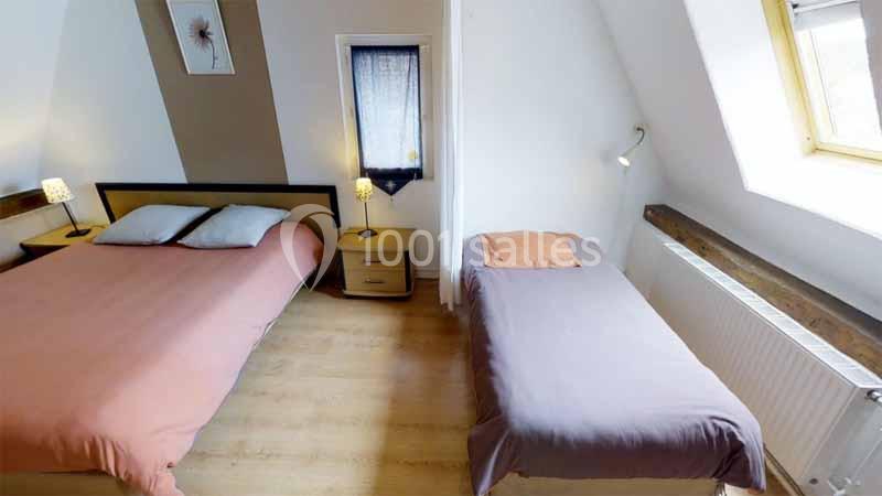 Chambre avec un lit double et un lit simple, éclairée par une fenêtre de toit et des lampes de chevet.