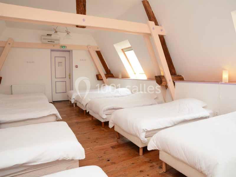 Dortoir lumineux avec plusieurs lits simples alignés, poutres apparentes et parquet en bois.