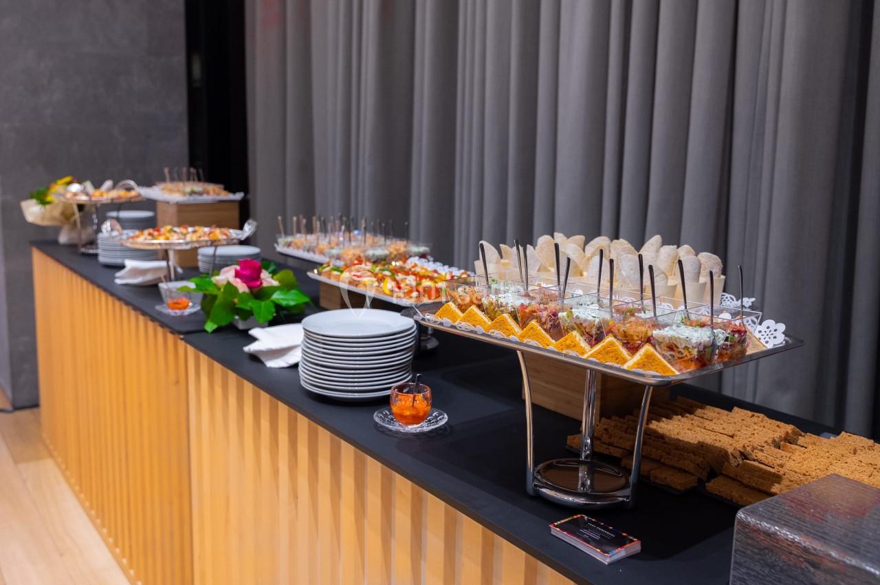 Buffet avec une variété de plats salés et sucrés, disposés sur une table avec des assiettes et des couverts à proximité.