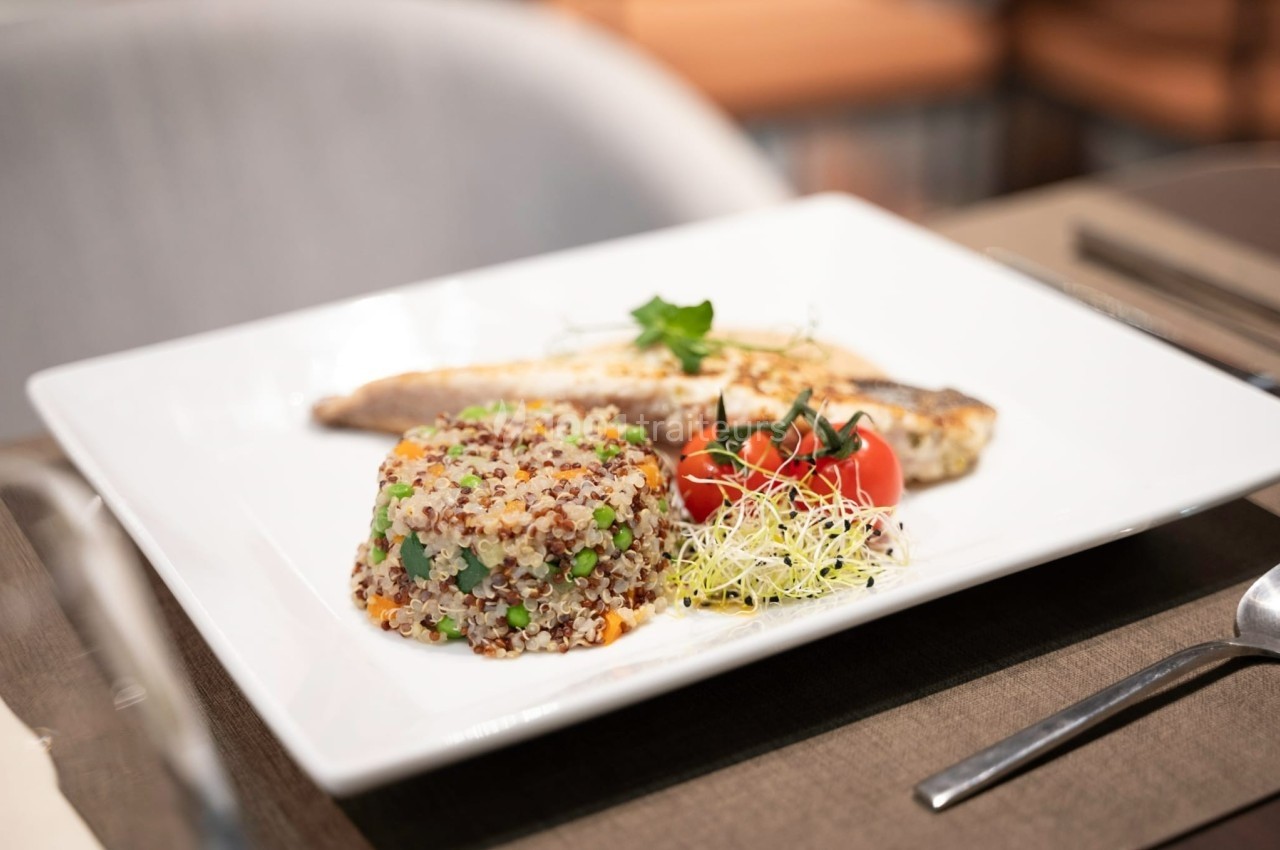 Assiette contenant du poisson grillé, un mélange de quinoa aux légumes, des tomates cerises et des pousses germées.
