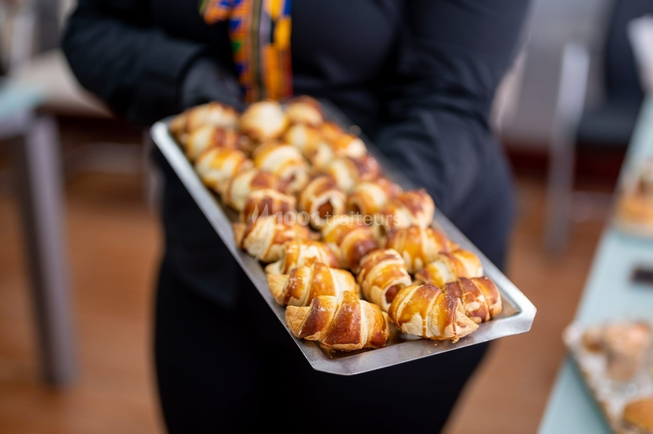 Plateau de petits croissants dorés et glacés, tenu par une personne vêtue de noir.