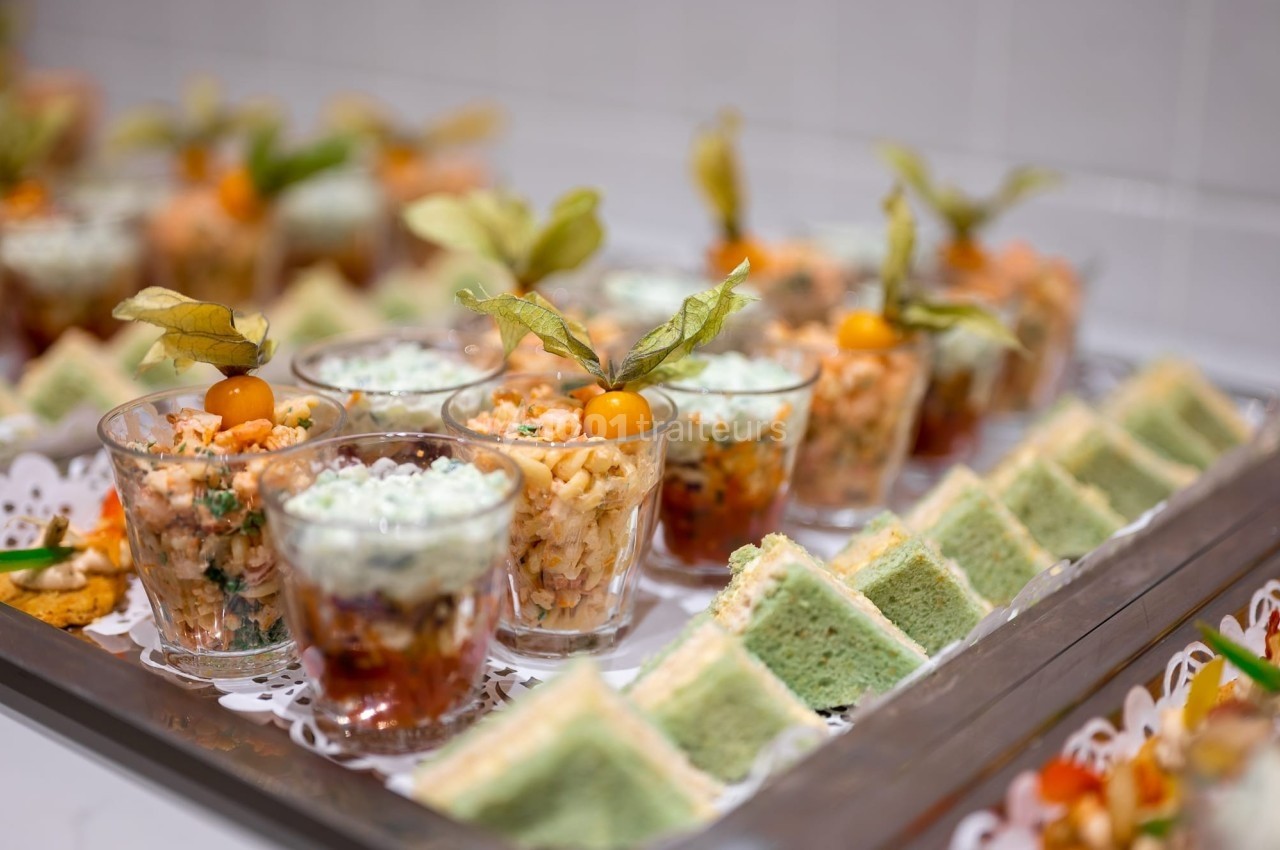 Plateau de verrines salées et de sandwichs triangulaires garnis, présenté sur un support décoratif.