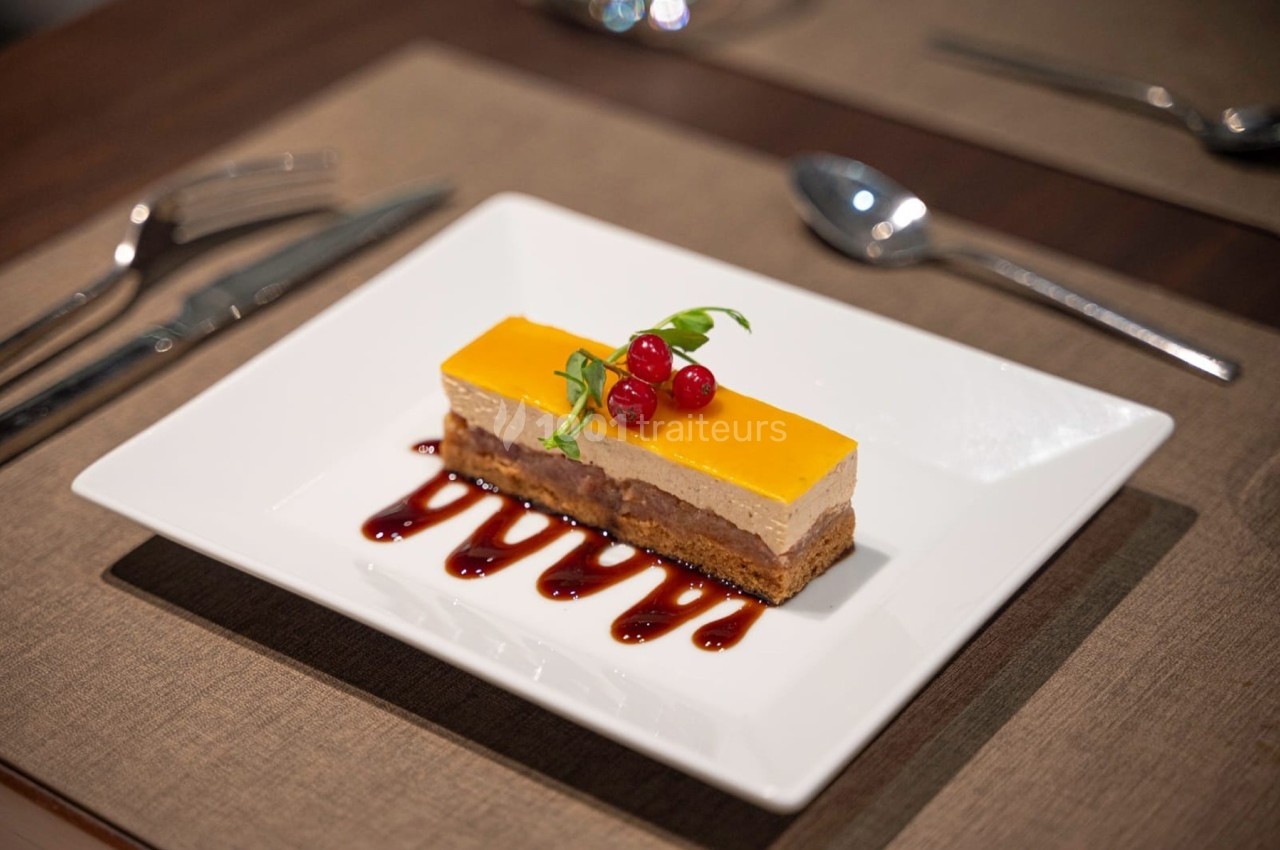 Dessert rectangulaire avec couches colorées, décoré de groseilles et servi sur un coulis rouge dans une assiette blanche.