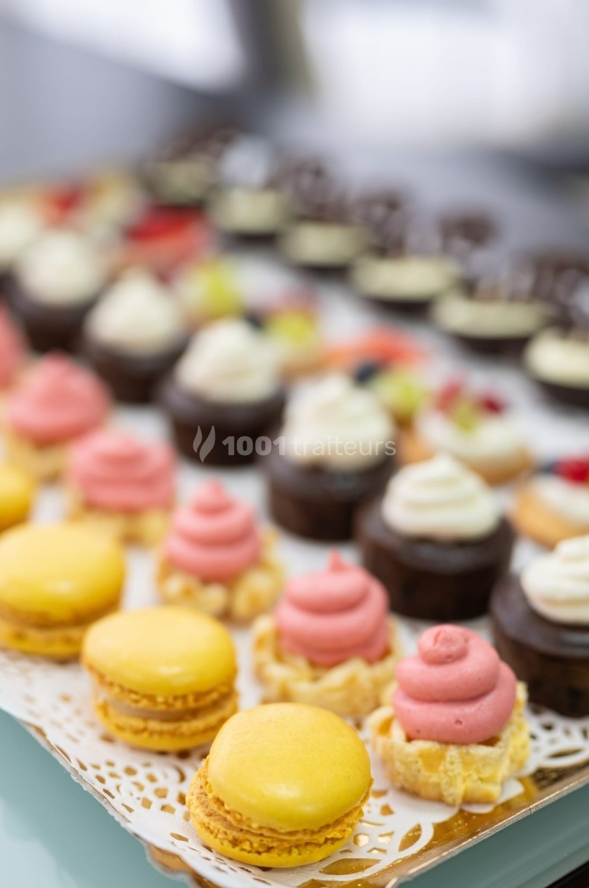 Plateau de pâtisseries variées comprenant macarons jaunes, tartelettes et petits gâteaux décorés de crème.