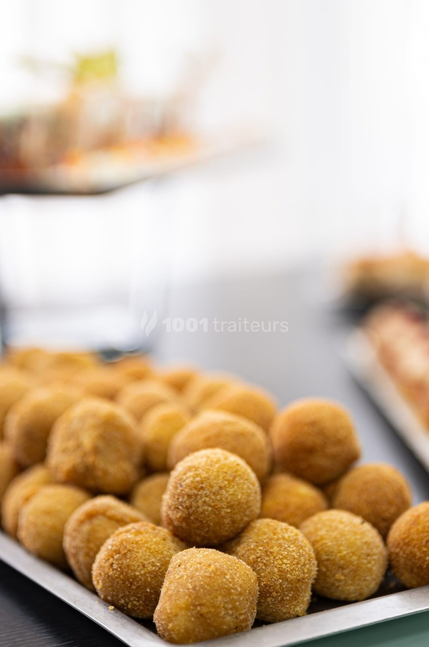 Plateau de boulettes panées dorées disposées en rangées, avec un fond flou de plats variés.