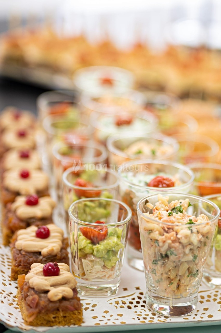 Plateau de verrines et bouchées apéritives variées, disposées sur un napperon décoratif.