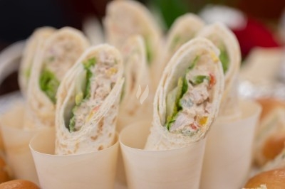 Assortiment de wraps garnis de légumes et de poulet, entourés de petits pains et de sandwichs sur un plateau.