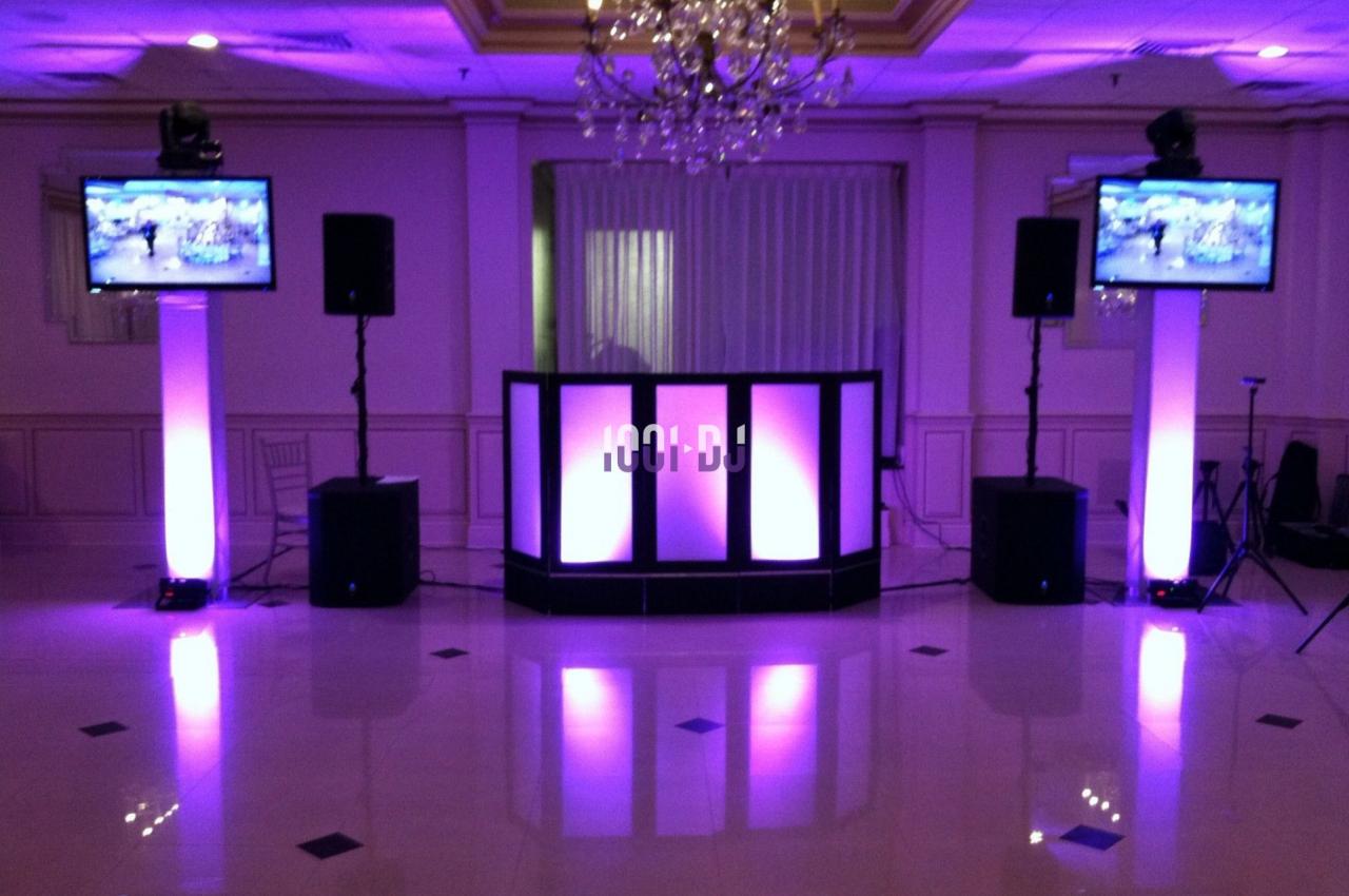 Installation de matériel audiovisuel avec éclairage violet, comprenant une table de mixage, haut-parleurs et écrans.