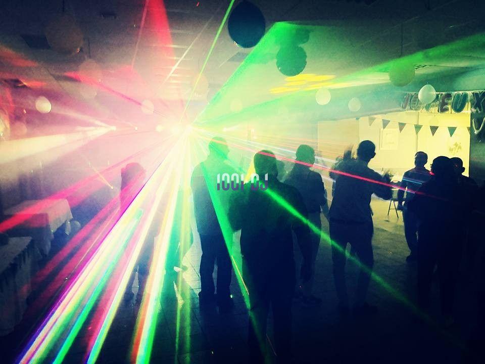 Personnes dansant dans une salle sombre éclairée par des faisceaux lumineux colorés et des effets de lumière.