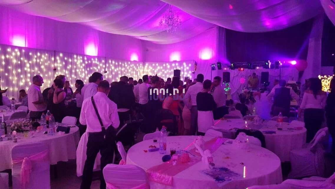 Salle de réception décorée avec des lumières violettes, des invités debout et assis autour de tables dressées.