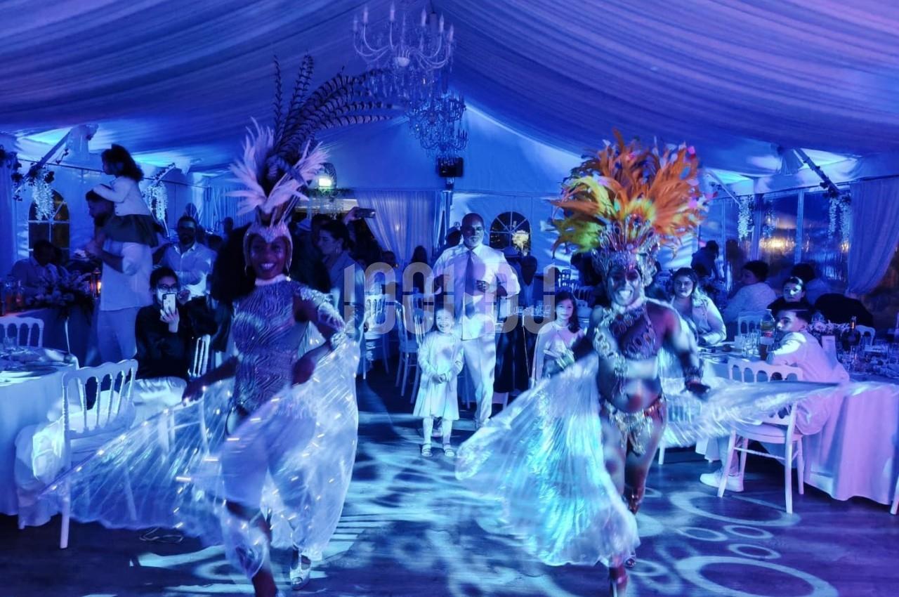 Danseuses en costumes colorés se produisant dans une salle éclairée de lumières bleues, entourées de convives attablés.