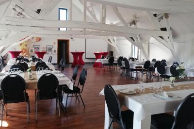 Salle lumineuse avec bar en bois, tables en verre, chaises noires et grandes fenêtres laissant entrer la lumière naturelle.