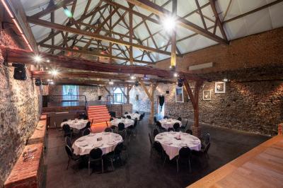 Salle en briques avec poutres apparentes, tables hautes noires et grandes ouvertures donnant sur un espace extérieur.