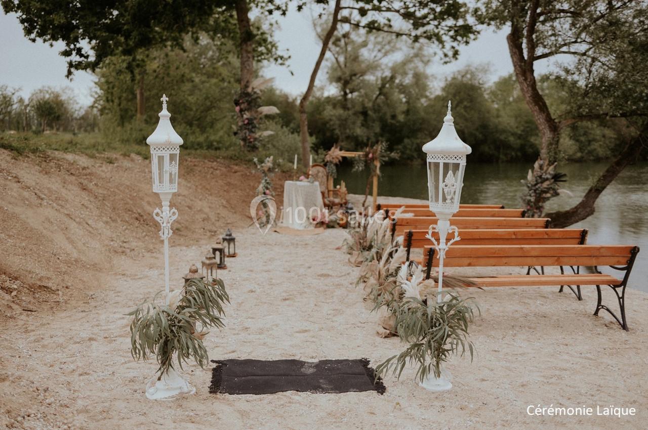 Allée décorée avec des lanternes blanches menant à un autel en plein air, entourée de bancs en bois et de verdure.