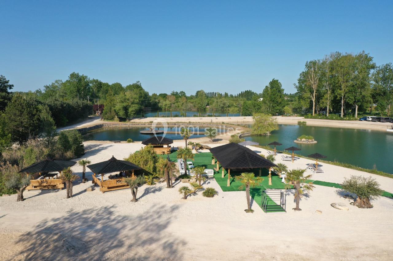 Vue aérienne d'un espace de loisirs avec plages de sable, palmiers, pergolas et étangs entourés de verdure.