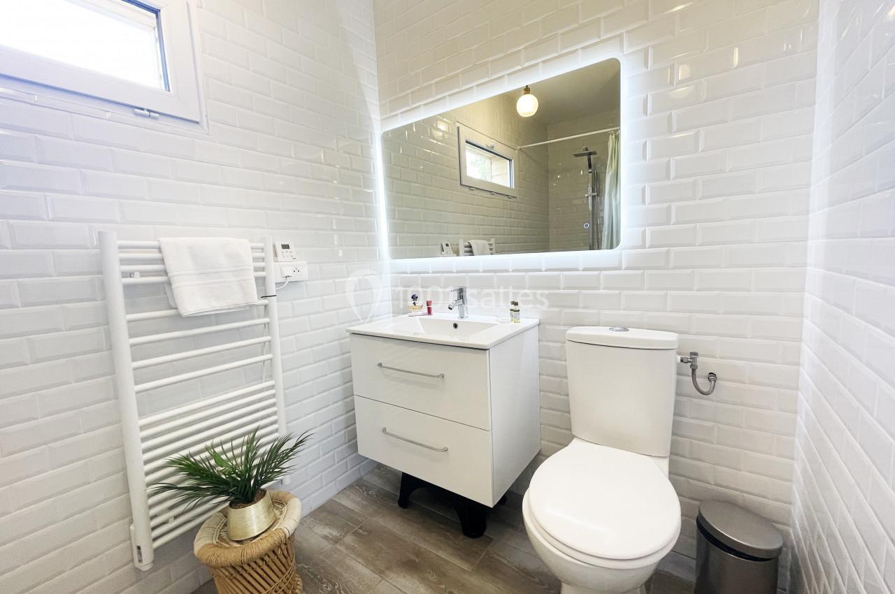 Salle de bain moderne avec carrelage blanc, meuble vasque, miroir éclairé, toilettes et radiateur mural.