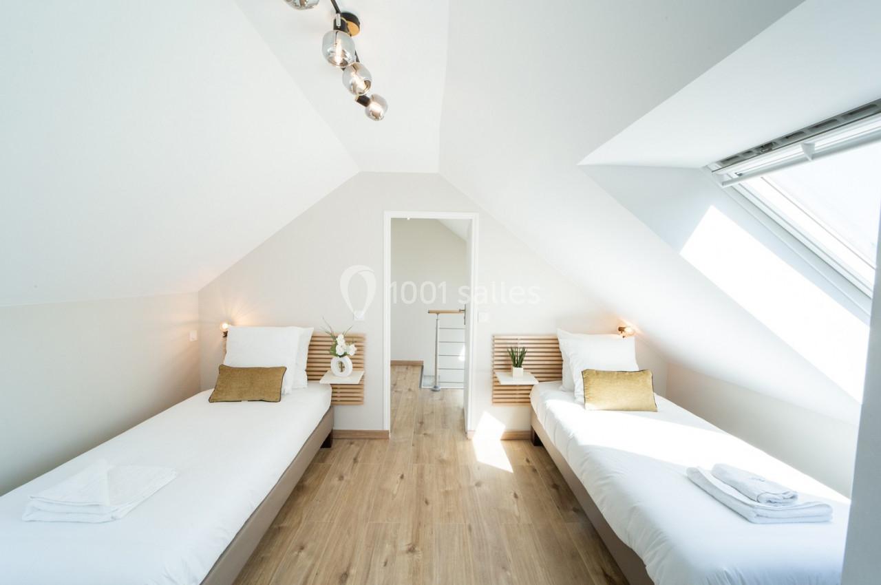 Chambre lumineuse avec deux lits simples, parquet au sol, fenêtre de toit et décoration minimaliste.
