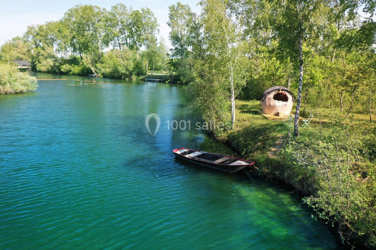 Barque amarrée sur une rivière bordée d'arbres, avec une tente installée sur la berge herbeuse.