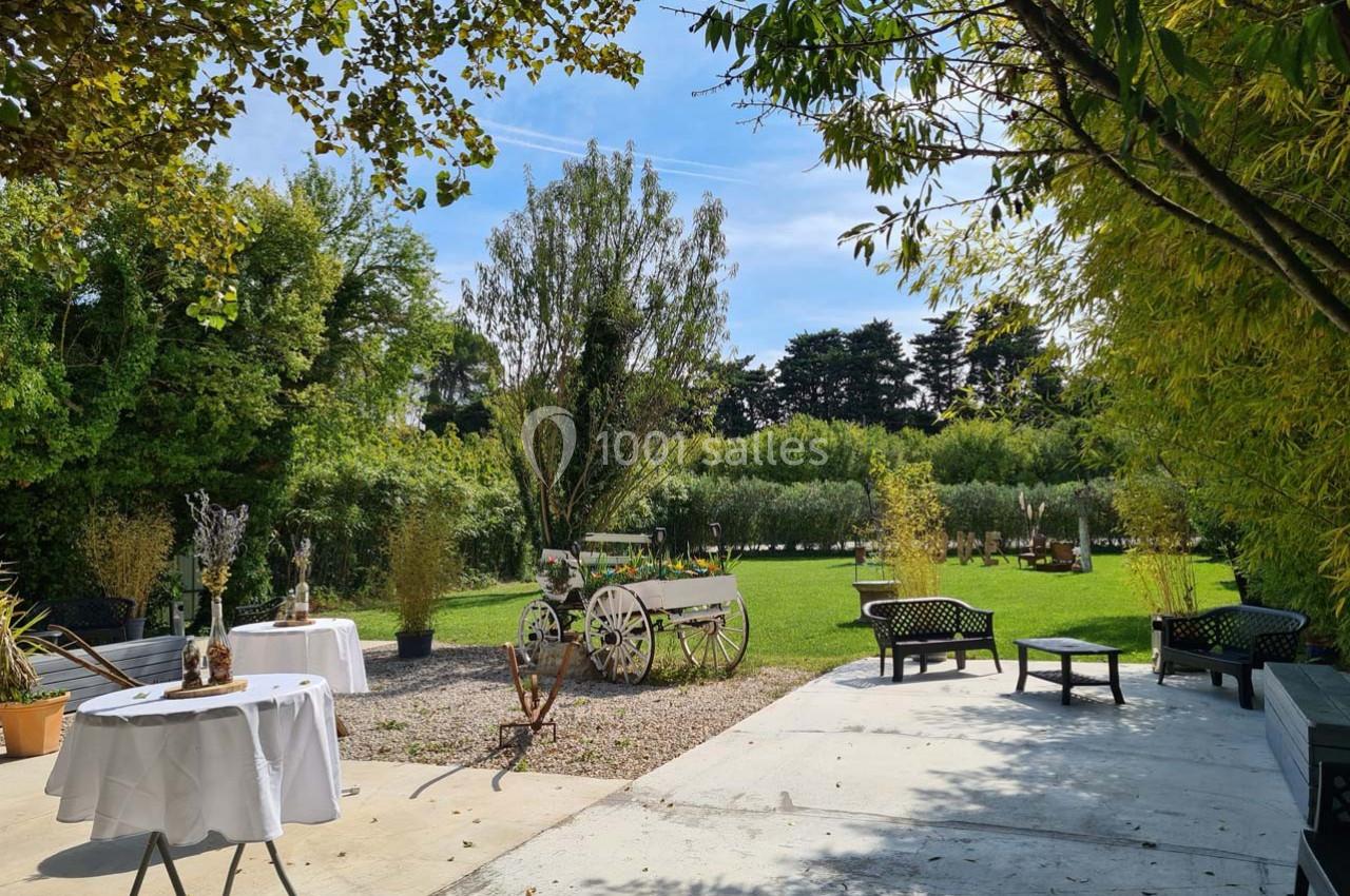 Jardin verdoyant avec pelouse, arbres, wagon décoratif et tables dressées sur une terrasse ensoleillée.