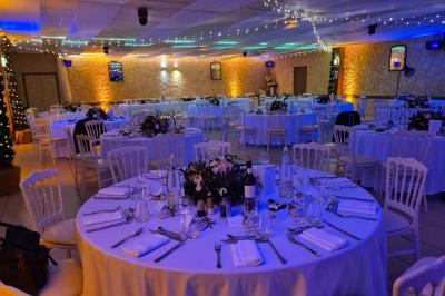 Salle vide avec un sol en parquet sombre, murs blancs, fenêtres et piliers gris sous un plafond à dalles blanches.