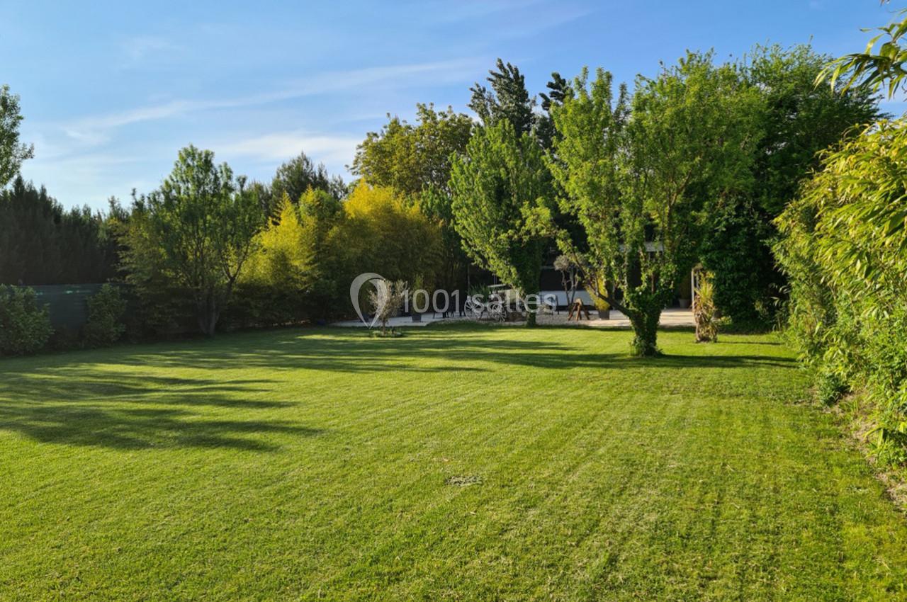Jardin verdoyant avec pelouse bien entretenue, arbres et arbustes sous un ciel bleu clair.