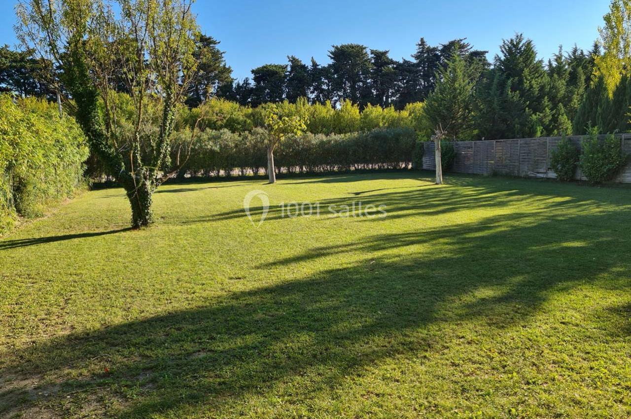 Pelouse verdoyante entourée d'arbres et de haies sous un ciel bleu clair.