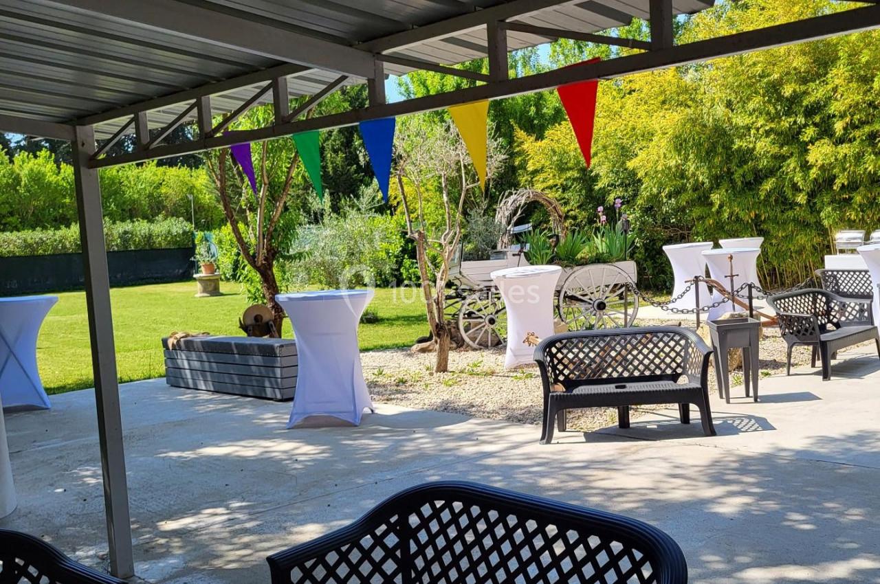 Espace extérieur avec tables hautes, bancs, charrette décorative et guirlande de fanions colorés sous un auvent.