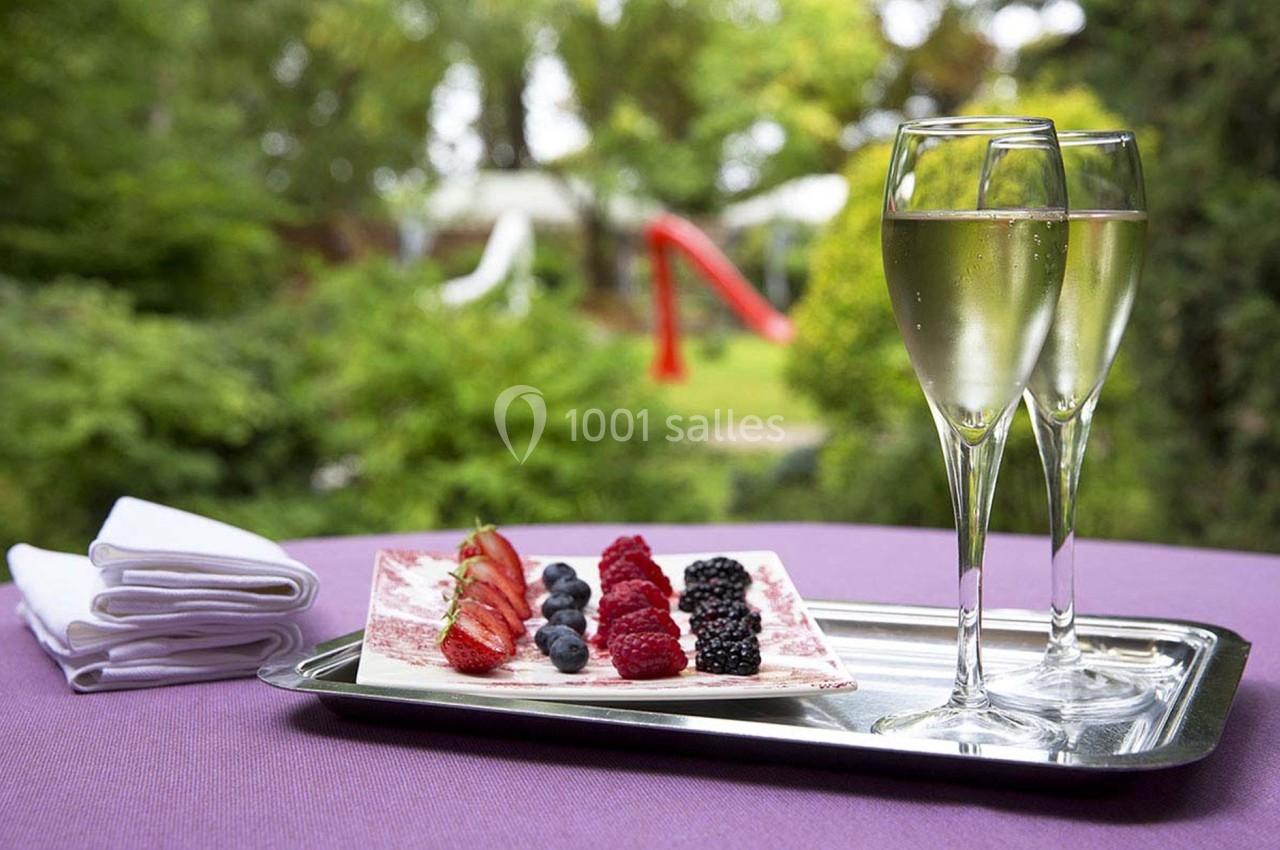 Deux coupes de champagne et une assiette de fruits rouges sur un plateau, posés sur une table en extérieur.