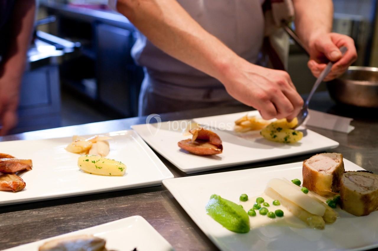 Un chef dresse des assiettes gastronomiques avec viande, légumes et purée dans une cuisine professionnelle.