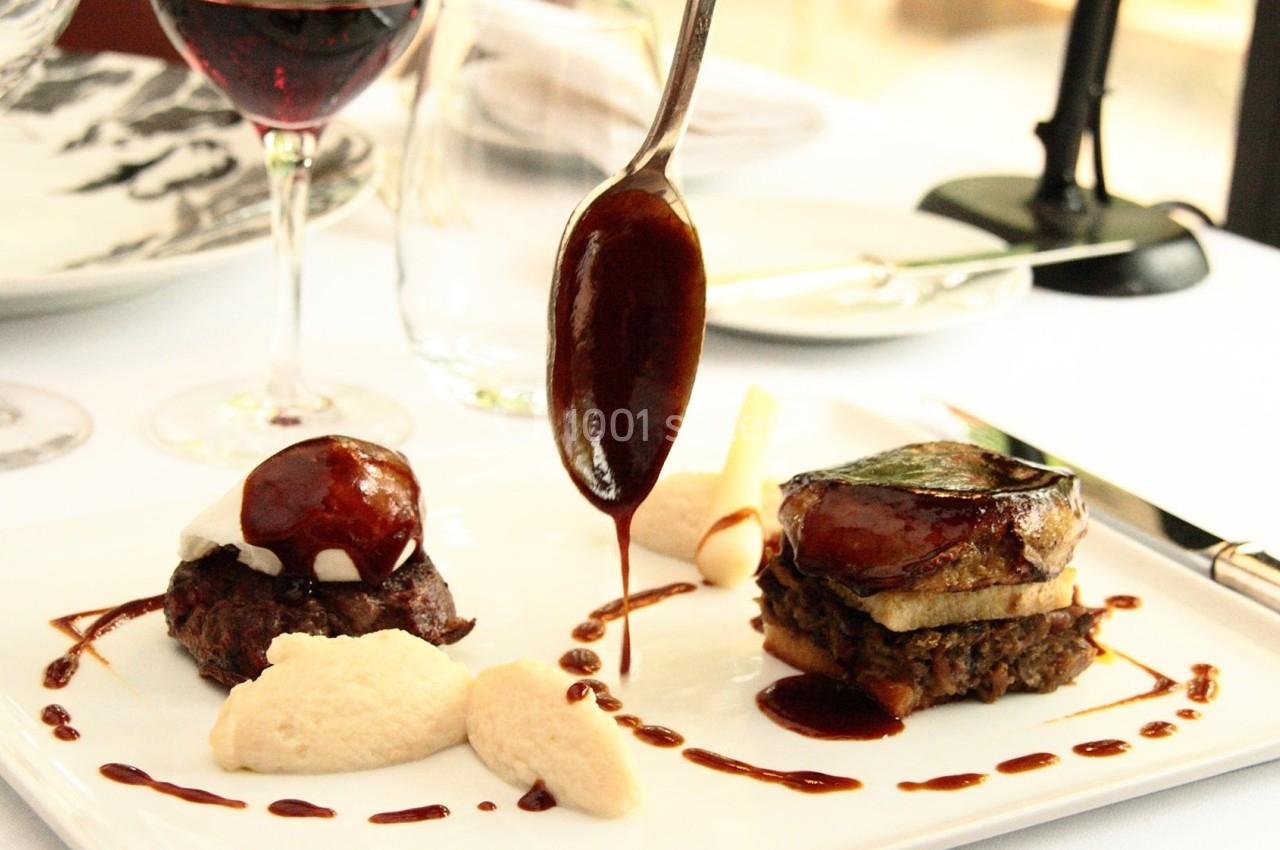 Assiette gastronomique avec viande, purée et sauce, servie sur une table dressée avec verre de vin et couverts.