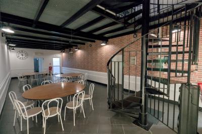Salle avec des tables rondes et des chaises blanches, éclairée par des lampes suspendues, avec un escalier en colimaçon au…